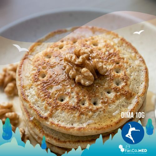 Un primo piano ravvicinato e dettagliato, in prospettiva macro, di un pancake con farina di mandorla e noci appena cucinato. Si vedono la superficie alveolata, il gheriglio di noce intero al centro e la finitura lucida del dolcificante liquido, con le altre porzioni sfocate sullo sfondo.
