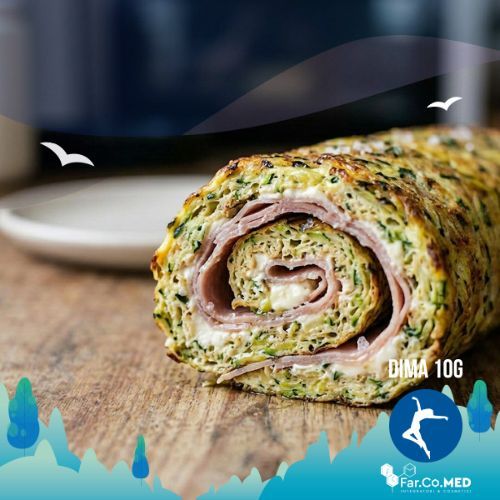 Vista ravvicinata di un rotolo di zucchine al forno intero e dorato su un piatto, con la sezione trasversale che mostra la spirale di farcitura al formaggio cremoso e prosciutto cotto.