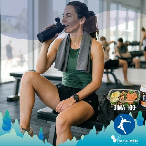 Una fotografia di un'atleta che riposa su una panca da palestra, simbolo dell'unione tra dieta chetogenica e sport. La donna beve da una borraccia nera mentre accanto a lei si trova un contenitore con un pasto tipico chetogenico a base di avocado e salmone. L'ambiente è una palestra luminosa con pesi e attrezzature sfocate sullo sfondo, trasmettendo un'atmosfera di salute e performance atletica autentica.