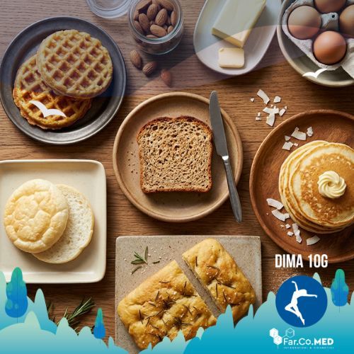 Una vista dall'alto di una ricca e invitante colazione senza carboidrati, ideale per la dieta chetogenica, disposta su un tavolo di legno rustico. L'immagine mostra cinque diverse alternative al pane: fette di mug bread tostato, chaffles croccanti, soffice cloud bread, una porzione di focaccia keto al rosmarino e pancake alla farina di cocco. Sono visibili anche ingredienti base come uova, burro, mandorle e rosmarino fresco.